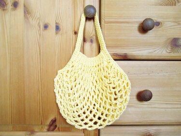 Gelbe gehäkelte Netztasche mit kurzem Henkel, an Holzknauf hängend
