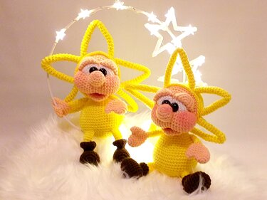 Two yellow crochet star amigurumi dolls with pink faces and brown boots on white fur beside star-shaped string lights