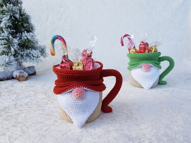 Gehäkelter Wichtelbecher in Rot mit Bonbons, im Hintergrund grüner Wichtelbecher, auf hellem Untergrund neben verschneigtem Tannenzweig
