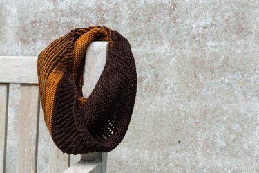 Gestrickter Loopschal in Braun und Orange auf einer Holzbank