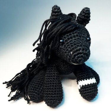 Schwarzes gehäkeltes Amigurumi-Pferd mit langer Mähne und weißem Streifen am Bein