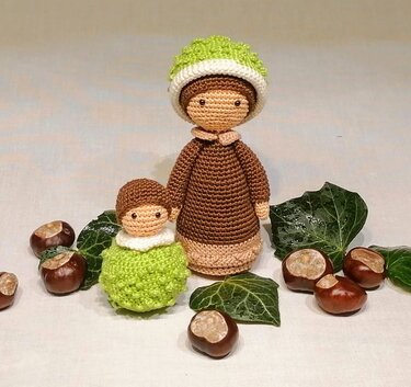 Zwei gehäkelte Amigurumi-Puppen in Braun und Grün, dekoriert mit Kastanien und Efeublättern
