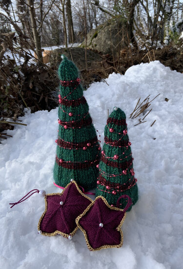 Gestrickte konische Tannen mit Perlenketten und zwei sternförmige Anhänger mit goldfarbenem Rand im Schnee