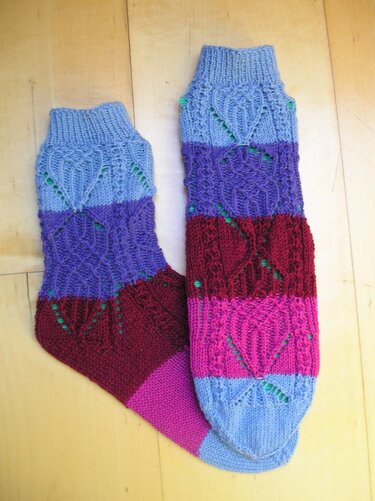 Zwei handgestrickte, mehrfarbige Damensocken mit Lochmustern auf Holzfußboden.