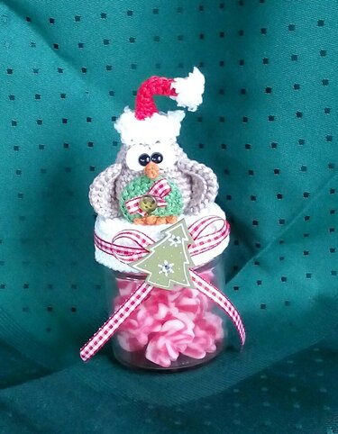Gehäkelte Weihnachtseule mit roter Mütze und Kranz auf einem festlich verzierten Glas voller Süßigkeiten