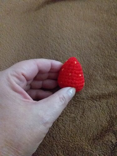 Person hält kleine, rot gehäkelte Erdbeere.