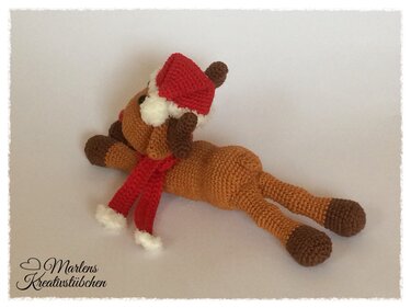 Liegendes gehäkeltes Amigurumi-Rentier mit roter Mütze und Schal
