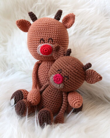 Zwei braune gehäkelte Rentier-Amigurumis mit roten Nasen auf hellem, flauschigem Untergrund