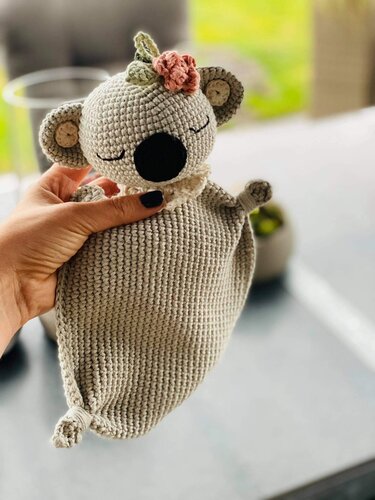 Detaillierte Ansicht eines handgehäkelten Koala-Schmusetuchs mit geschlossenen Augen und einer Blume auf dem Kopf.