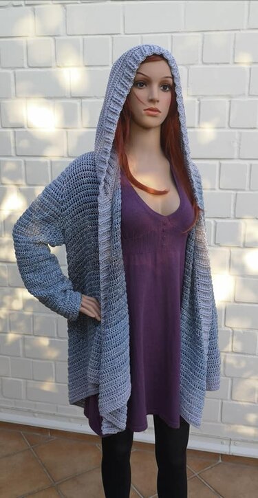 Schaufensterpuppe zeigt offen getragene gehäkelte Kapuzenjacke in Blau‑Grau-Ombré über violettem Kleid