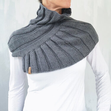 Person wearing a charcoal-gray ribbed knitted collar scarf with a rolled high neck over a white long-sleeve top