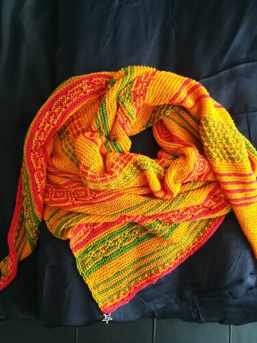 Gestricktes Dreieckstuch in Gelb, Orange und Grün mit Streifen und kleinen Lochmustern, zusammengerollt auf dunklem Stoff