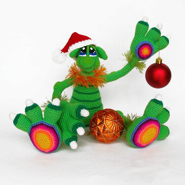 Green amigurumi dragon wearing a Santa hat with rainbow paw pads and Christmas baubles