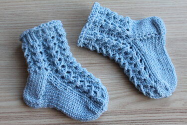 Hellblaue gestrickte Babysocken mit Ajourmuster auf hellem Holzuntergrund