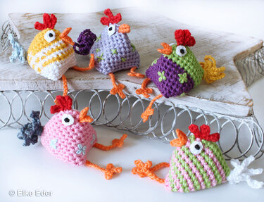 Fünf bunte gehäkelte Amigurumi-Hühner auf Holzbrett