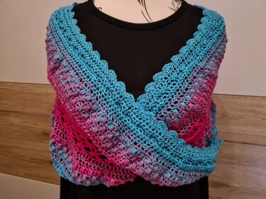 Gehäkelter Loop in Pink und Türkis mit Bobbelmuster und gewellter Kante, drapiert über eine schwarze Büste
