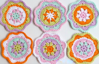 Sechs pastellfarbene gehäkelte Blumen-Applikationen mit Muschelrand