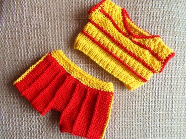 Handgestricktes gelb-rotes Puppen-Top und passender Rock auf hellem Untergrund