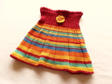 Gestrickter Kinderrock mit bunten Querstreifen in Regenbogenfarben, rotem Rippenbund und gelber Häkelblume.