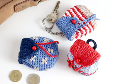 Three crocheted items: a striped key pouch, a blue floral coin pouch, and a red-and-blue mini backpack charm with a key and coins.