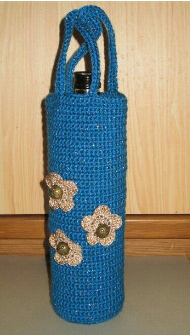 Handgehäkelte blaue Flaschenhülle mit zwei Griffen und drei beigen Blumenapplikationen