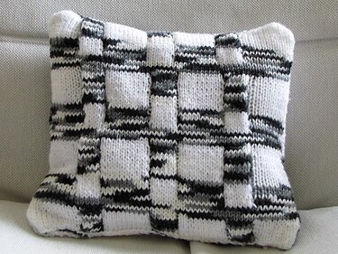 Gestricktes Kissen mit quadratischem Gittermuster in Schwarz, Weiß und Grau auf hellem Sofa