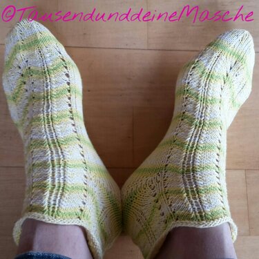Gestrickte Socken in hellgelben und lindgrünen Streifen auf hellem Holzboden