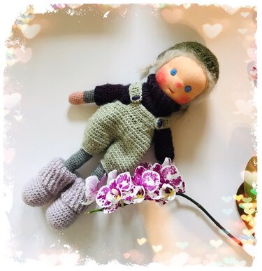 Gehäkelte Amigurumi-Puppe mit Mütze, Latzhose und Stiefeln neben Orchideen