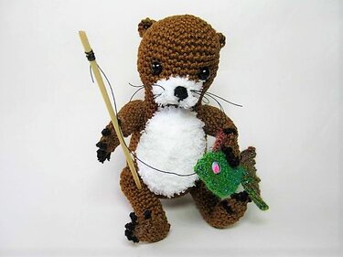Gehäkelter brauner Otter-Amigurumi mit weißem Bauch, Angelrute und grünem Fisch
