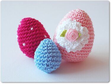 Drei Amigurumi-Ostereier gehäkelt in Magenta, Hellblau und Rosa mit weißer Häkelblüte