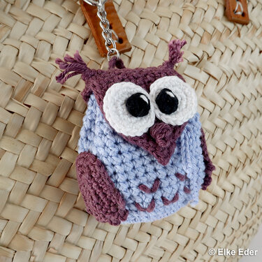 Crocheted owl keychain in lavender and plum attached to a woven bag