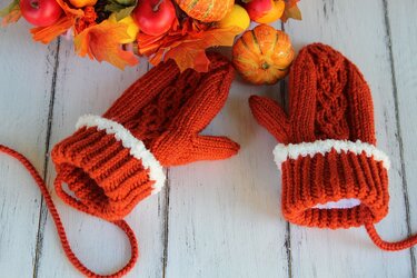 Orange knit mittens with white fluffy cuff trim styled with small pumpkins and autumn leaves