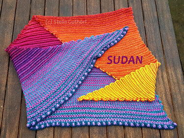 Colorful crocheted triangle shawl with orange, fuchsia, purple, teal and yellow stripes on a wooden background.