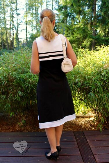 Frau von hinten in zweifarbigen, ärmellosen Kleid mit weißen und schwarzen Elementen vor natürlichem Hintergrund