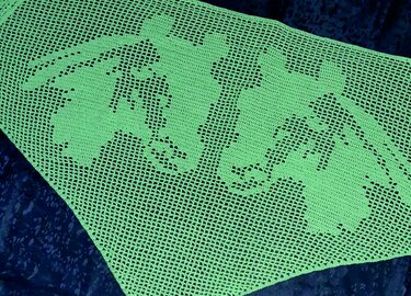 Hellgrünes gehäkeltes Tuch mit Hasen-Filetmuster auf dunklem Untergrund.