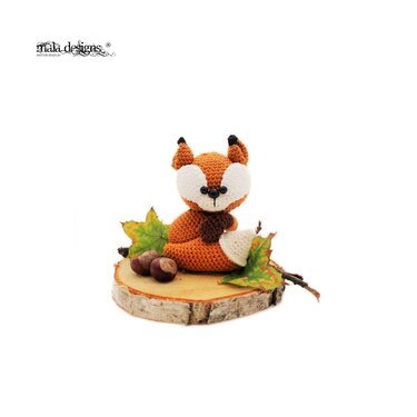Gehäkelter Amigurumi-Fuchs in Orange und Weiß auf einer Holzscheibe mit Kastanien