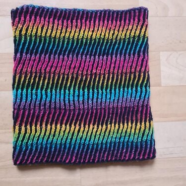Gestrickter Loop-Schal mit schmalen vertikalen Rippen in Regenbogenfarben auf dunklem Grund