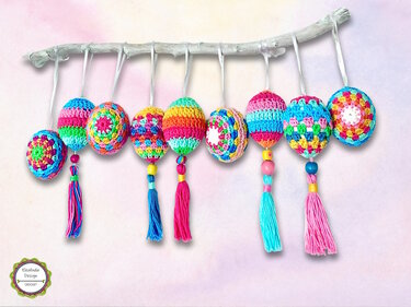 Colorful crocheted egg ornaments with tassels and beads hanging from a branch.