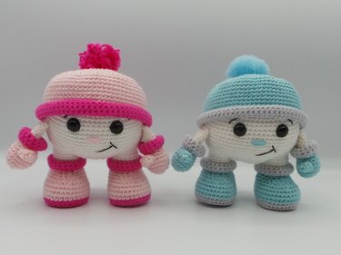 Zwei Amigurumi-Püppchen in Rosa und Hellblau mit Bommelmützen