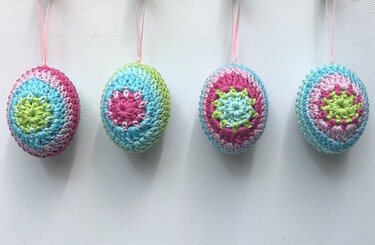 Four pastel crocheted Easter egg ornaments with star motifs and pink ribbons on a white background.