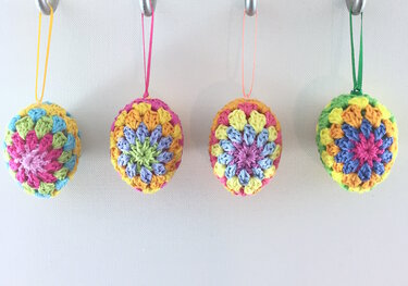 Four pastel crochet Easter egg ornaments with colored ribbon hangers on hooks