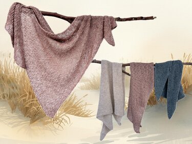 Vier gestrickte Tücher an Ästen vor Dünen mit Strandgras: großes mauvefarbenes Dreieckstuch, beiges Tuch, weiteres mauvefarbenes Tuch und ein blaues Tuch.