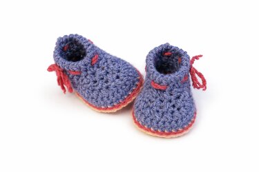 Gehäkelte lila Babyschuhe mit rosafarbenen Akzenten nebeneinander