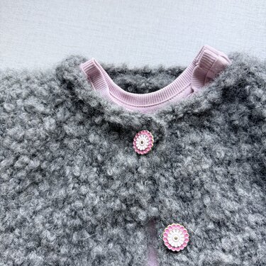 Kuschelige graue Kinderjacke aus Bouclé mit rosa Blumenknöpfen über rosa Oberteil