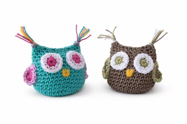 Zwei gehäkelte Amigurumi-Eulen, eine türkis mit rosa Augen, eine braun mit grünen Augen, vor weißem Hintergrund.