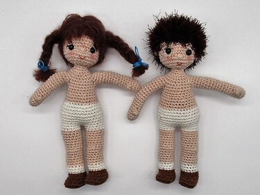 Zwei gehäkelte Amigurumi-Puppenrohlinge, Junge mit kurzem dunklem Haar und Mädchen mit Zöpfen, beide in weißer Unterwäsche
