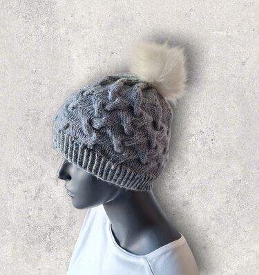 graue Strickmütze mit Rippbund, Zopfmuster und hellem Bommel auf Schaufensterkopf
