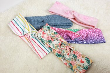 Mehrere Stirnbänder in unterschiedlichen Breiten und Mustern (Streifen, Blumen, Glitter-Farbverlauf, gestrickt) auf hellem Hintergrund.
