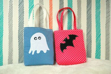 Zwei Stofftaschen für Halloween: blau mit weißem Geist und rot gepunktet mit schwarzer Fledermaus.