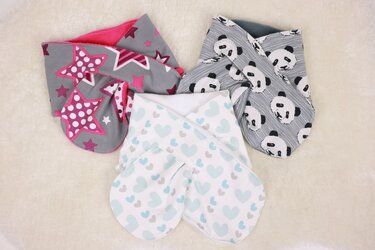 Drei farbenfrohe Loop-Schals für Kinder: grau mit pinken Sternen, weiß mit blauen Herzen und grau mit Panda-Muster auf hellem, flauschigem Untergrund.